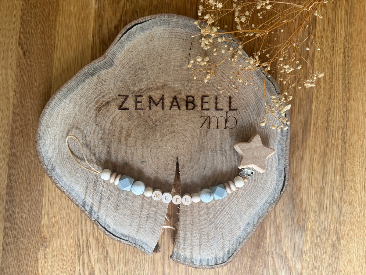 Personalisierbare Schnullerkette mit Holzbuchstaben und einem Stern in sanften Farben auf Holzuntergrund.