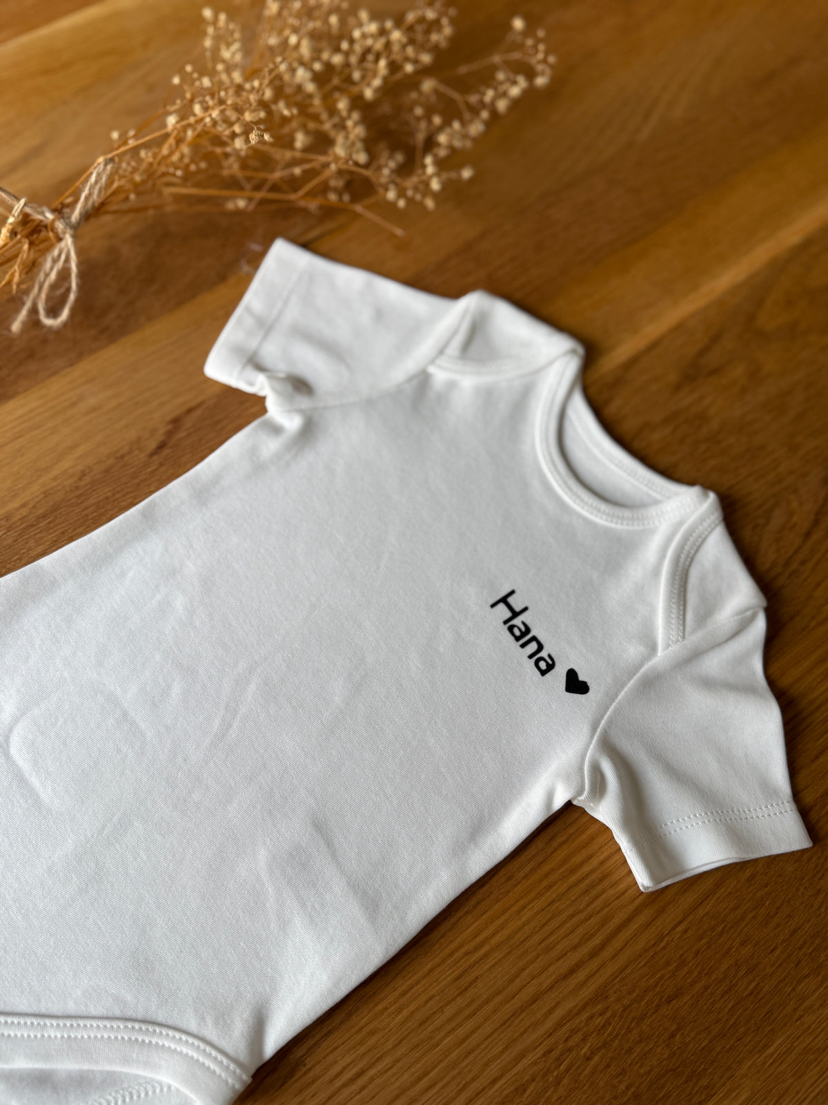 Personalisierbarer Babybody aus Bio-Baumwolle mit dem Namen 'Hana' und Herzsymbol, ideal als Geschenk.