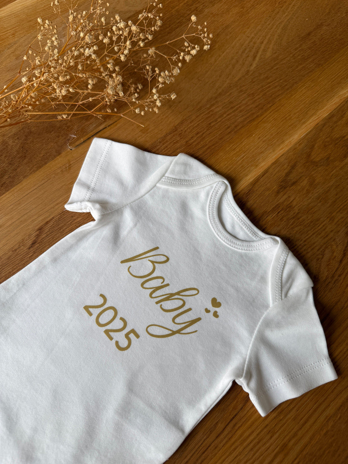 Personalisierbarer Baby-Body aus Bio-Baumwolle mit dem Geburtsjahr 2025 in goldener Schrift.
